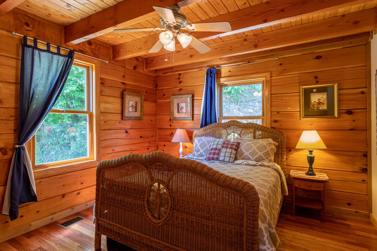 A warm and inviting bedroom with a wicker bed frame, soft window curtains, bedside table lamps, and framed artwork, creating a tranquil atmosphere ideal for restful retreats.