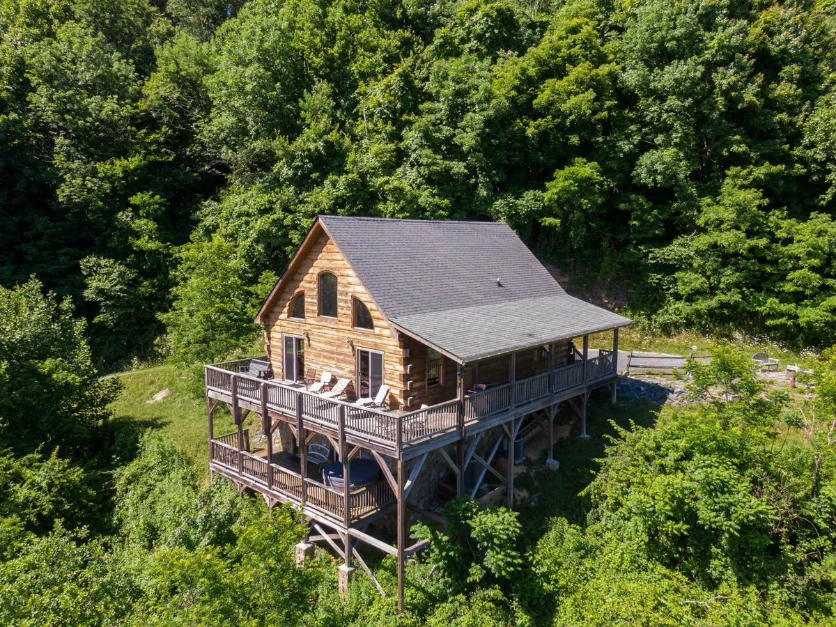 The hero image showcases a charming wooden cabin nestled amidst lush North Carolina greenery, with an expansive deck that invites guests to relax and soak in the scenic mountain surroundings. The image highlights the tranquil setting, the spacious outdoor living area perfect for gatherings or peaceful mornings, and hints at activities like stargazing and enjoying the fresh mountain air.