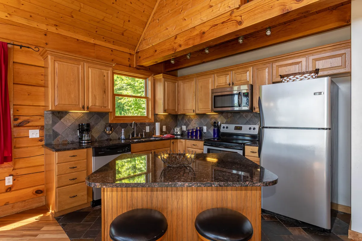 An inviting chef’s kitchen with a central island, gleaming stainless steel appliances, warm wooden cabinetry, and generous windows letting in natural light. The space is set for entertaining, with ample room for meal preparation and socializing, perfectly blending function and style.