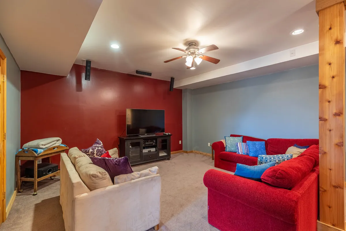 The room features a red couch, a white couch, a TV, and a ceiling fan, all arranged in a cozy, inviting manner. This is clearly a family-friendly entertainment room, ideal for watching movies or playing games together.