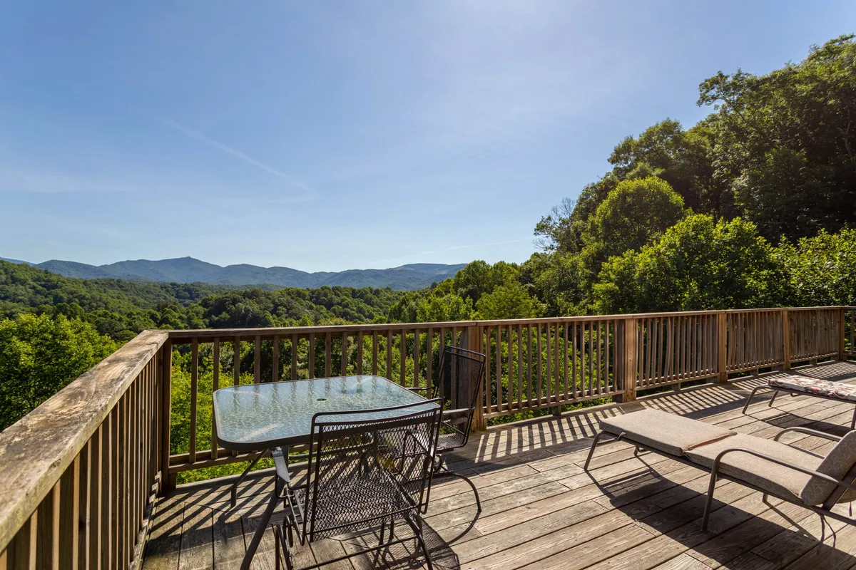A wooden deck with comfortable outdoor furniture overlooks a breathtaking mountain view. The scene is peaceful and inviting, with the deck positioned perfectly to enjoy both sunrise and stargazing. The setting suggests a private and serene place to savor morning coffee or relax under the stars, directly connecting guests with the natural surroundings.