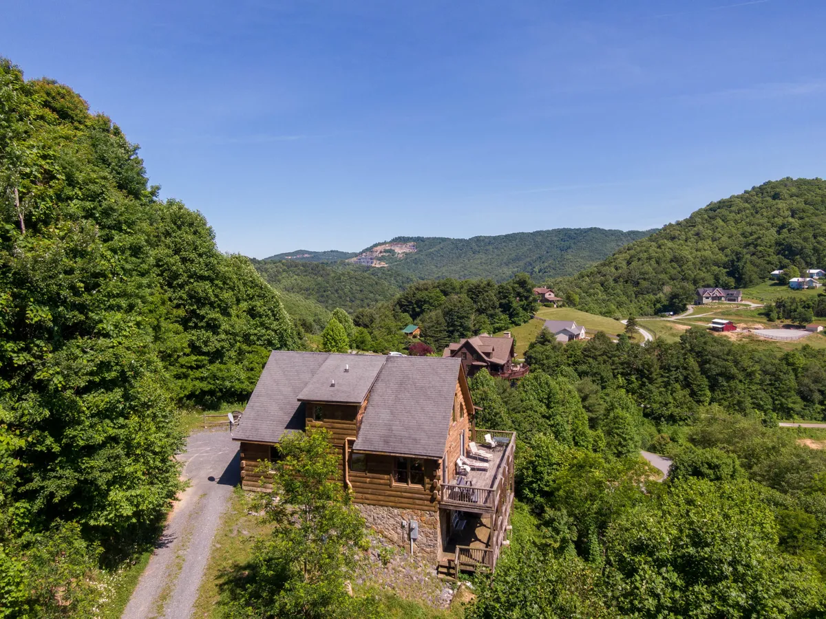 This image showcases the log cabin structure nestled amidst lush greenery with a mountain backdrop and an inviting deck area. The scene captures the cabin’s integration with the natural landscape, suggesting easy access to hiking trails, outdoor activities, and a peaceful environment for group gathering.